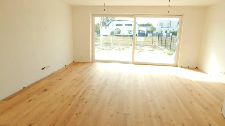 Helles, unmöbliertes Wohnzimmer mit Holzboden und Zugang zur Terrasse.