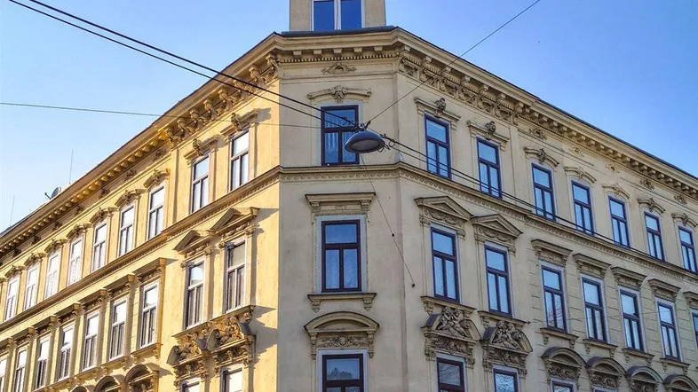 Historisches Eckgebäude mit reich verzierten Fassaden und klassischen Fenstern unter blauem Himmel.