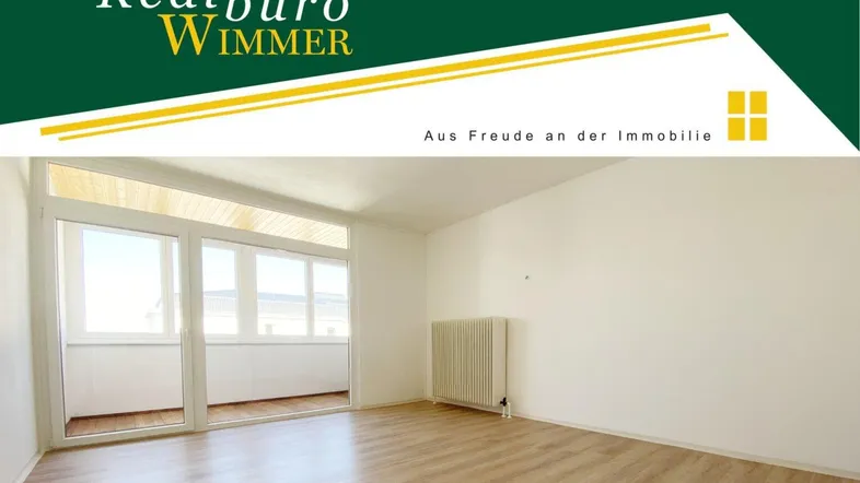 Heller, leerer Wohnraum mit großen Fenstern, Laminatboden und Zugang zu einem Balkon.
