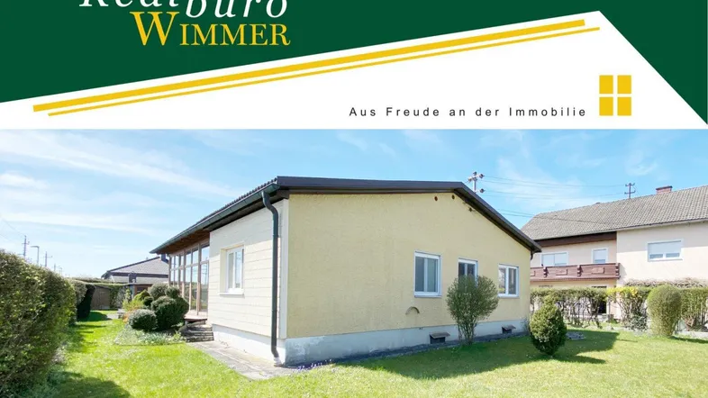 Gelbes Einfamilienhaus mit gepflegtem Rasen und Firmenlogo im oberen Bereich.