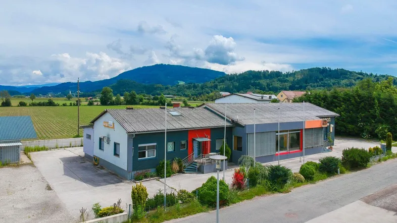 Luftaufnahme des Geschäftsgebäudes mit umliegender Landschaft und Bergen im Hintergrund unter bewölktem Himmel.