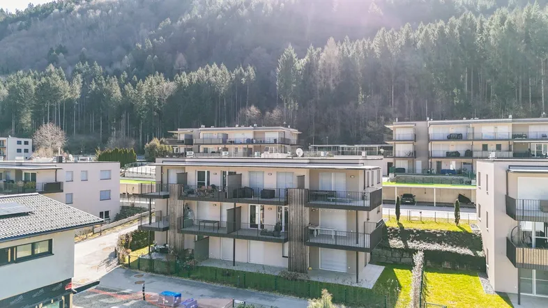 Moderne Wohnanlage mit mehreren Gebäuden am Waldrand und Bergblick.