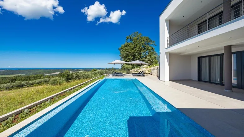 Moderner Infinity-Pool mit atemberaubendem Blick auf die grüne Landschaft und das Meer.