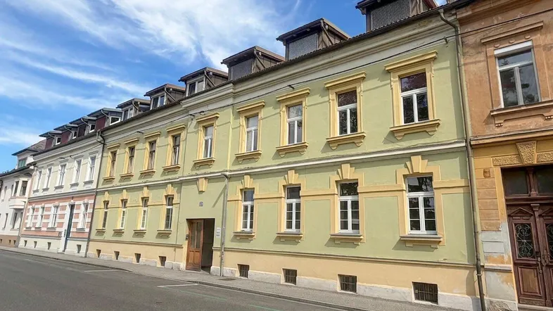 Mehrstöckiges Gebäude mit gelb-grüner Fassade, vielen Fenstern und Dachgauben an einer Straße.