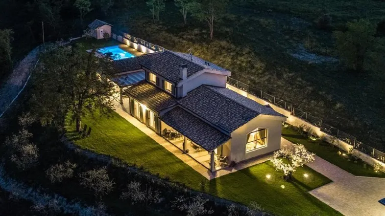 Nachtaufnahme einer luxuriösen Villa mit beleuchtetem Pool und weitläufigem Grundstück in ländlicher Umgebung.