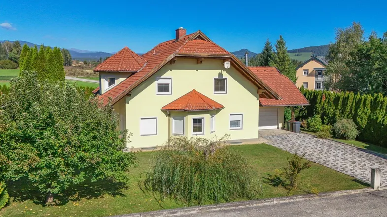 Freistehendes Einfamilienhaus mit gelber Fassade, rotem Ziegeldach und gepflegtem Vorgarten.