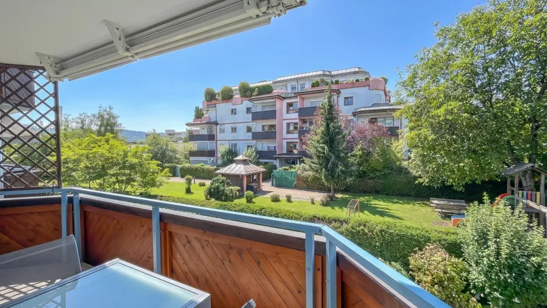 Geräumiger Balkon mit Sitzgelegenheiten und Blick auf die gepflegte Gartenanlage und das Wohngebäude.