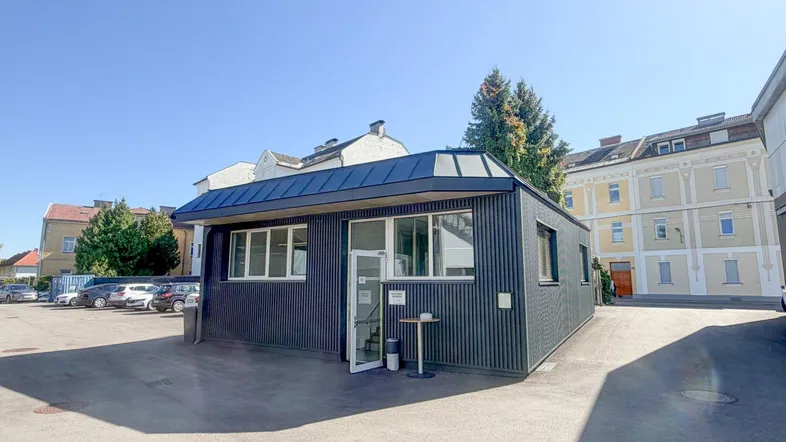 Modernes, freistehendes Bürogebäude mit dunkler Fassade und Parkplätzen im Freien.