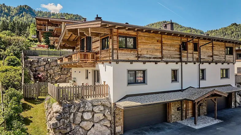Modernes Chalet mit Holzfassade und weißem Putz, eingebettet in eine Berglandschaft mit Garagen.