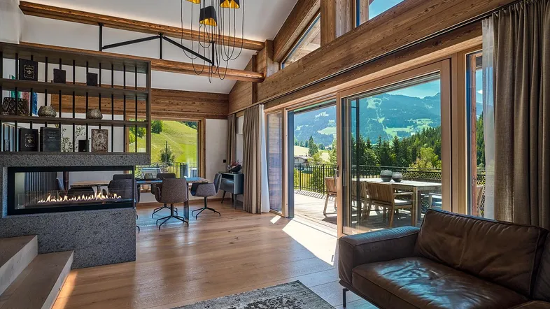 Geräumiges Wohnzimmer mit modernem Kamin, Holzbalken und atemberaubendem Bergblick von der Terrasse.