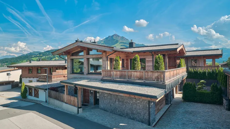 Moderne Chalet-Architektur mit Holzfassaden, Balkonen und beeindruckendem Bergblick unter blauem Himmel.