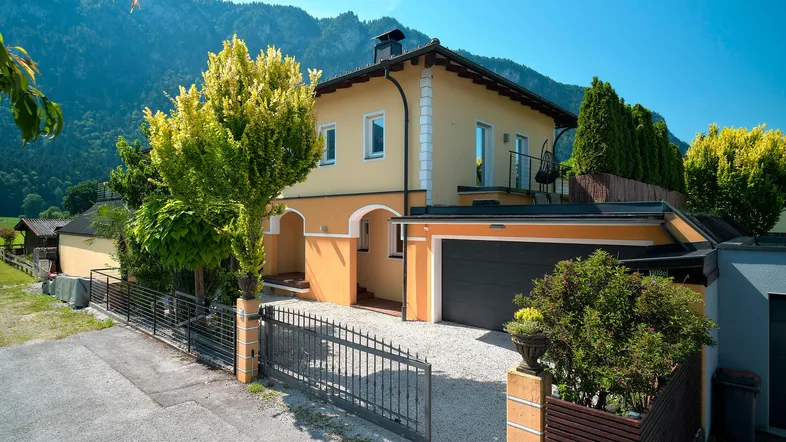 Einfamilienhaus mit Bergblick, integrierter Garage und gepflegtem Vorgarten unter blauem Himmel.