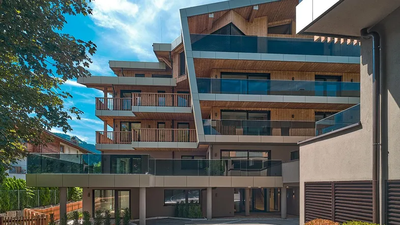 Modernes Apartmentgebäude mit Holzfassade, Glasbalkonen und grüner Umgebung unter blauem Himmel.