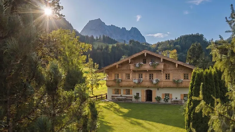 Traditionelles Holzhaus im alpinen Stil mit Balkonen und beeindruckendem Bergblick in sonniger Umgebung.