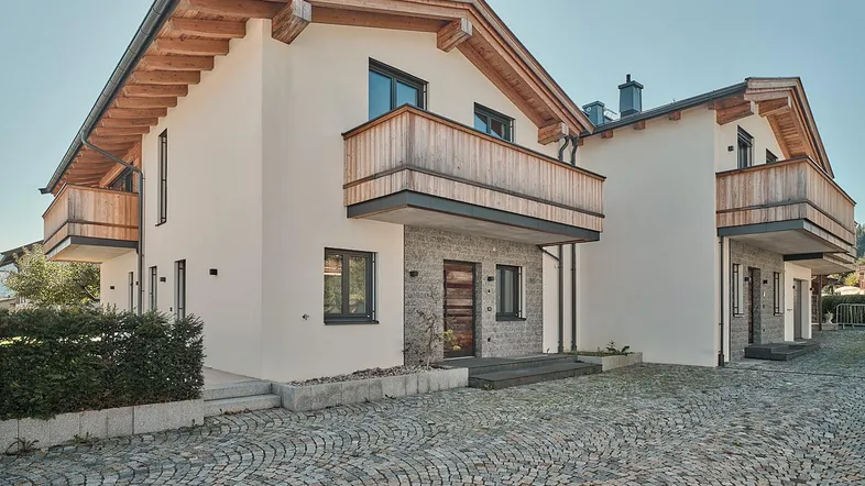 Moderne Chalet-Gebäude mit Holzbalkonen und Steinfassade, umgeben von einem gepflasterten Hof.