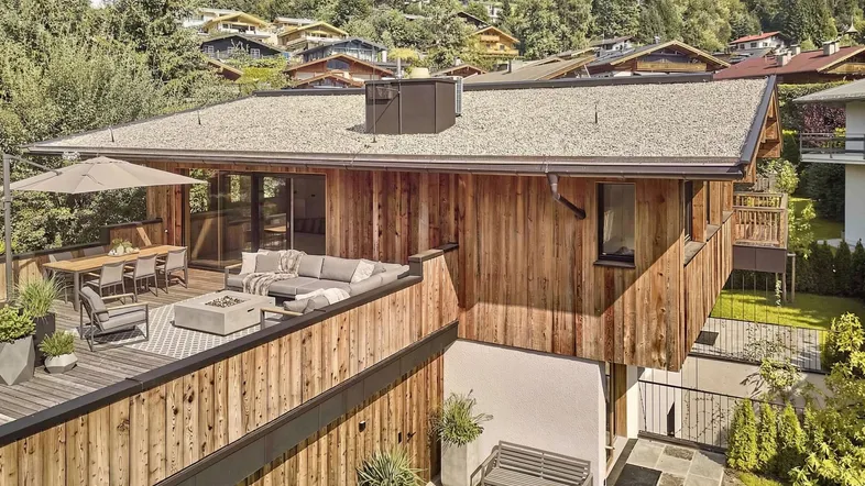 Modernes Chalet mit großer Dachterrasse, Essbereich und Lounge-Möbeln sowie Blick auf die umliegende Berglandschaft.