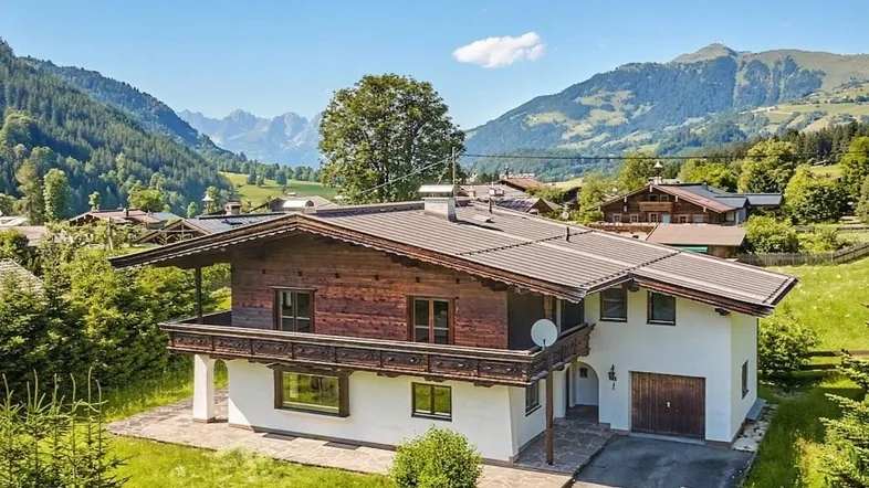 Traditionelles Chalet mit Holzbalkonen und weißer Fassade vor alpiner Bergkulisse.