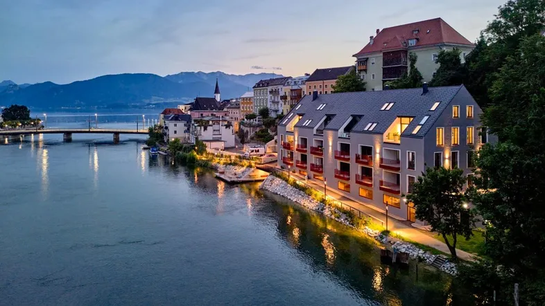 Moderne Gebäude am Flussufer bei Sonnenuntergang mit Bergblick und Stadtkulisse.