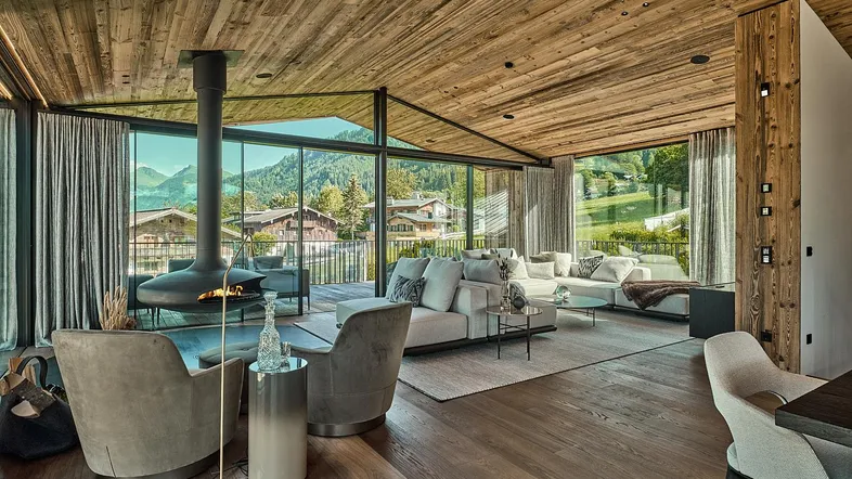 Geräumiges Wohnzimmer mit Holzbalkendecke, modernem Kamin und raumhohen Fenstern mit Bergblick.