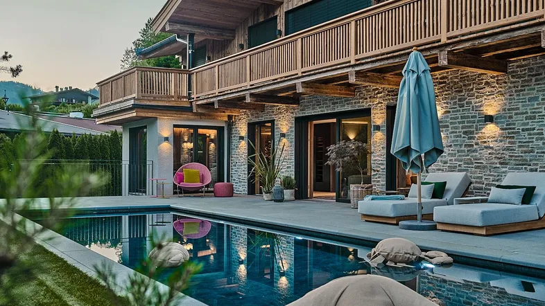 Luxuriöser Außenbereich mit großem Pool, bequemen Liegen und traditioneller Holzfassade des Hauses.