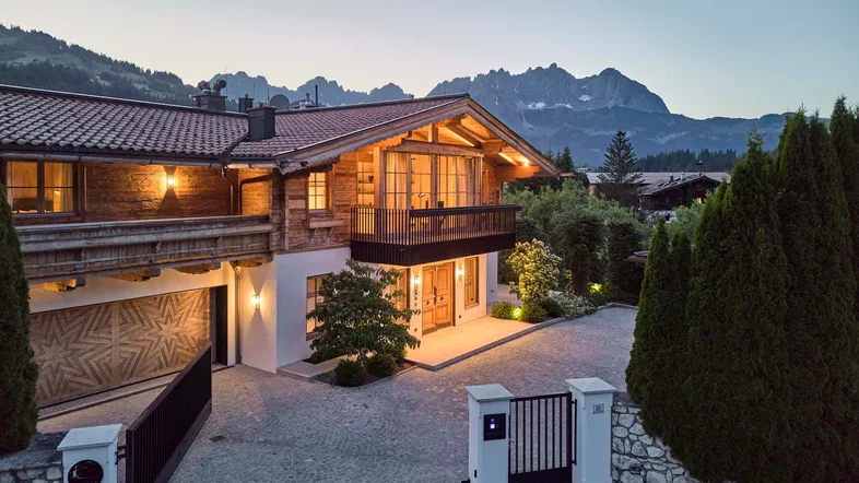 Luxuriöses Chalet mit traditioneller Holzfassade, Balkonen und Bergblick bei Sonnenuntergang.