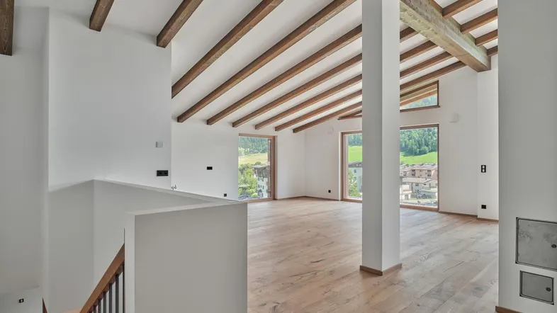 Geräumiger Wohnbereich mit hohen Decken, sichtbaren Holzbalken und großen Fenstern mit Bergblick.