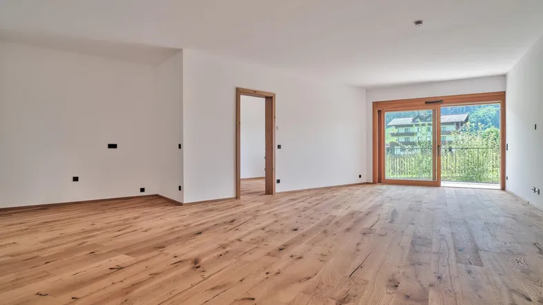 Heller, unmöblierter Wohnbereich mit hochwertigem Holzboden und Zugang zu einem Balkon mit grüner Aussicht.
