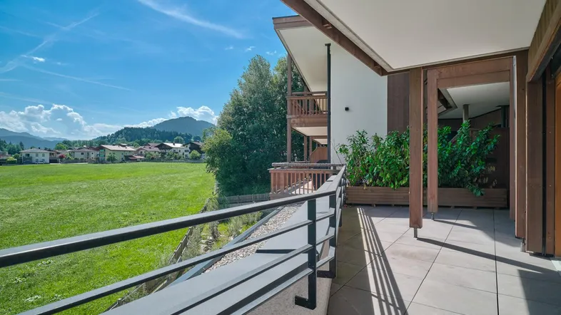 Geräumiger Balkon mit Fliesenboden, Metallgeländer und weitem Blick über grüne Felder und Berge.