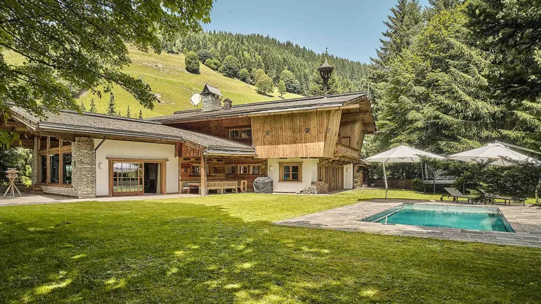 Großzügiges Chalet mit Außenpool und weitläufigem Garten, umgeben von grünen Hügeln und Wäldern.