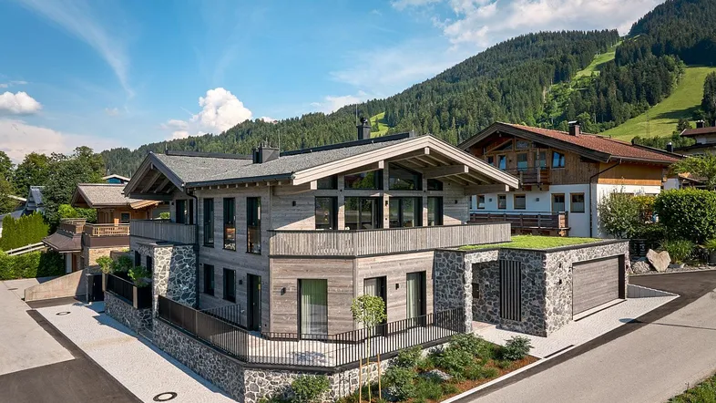 Modernes Chalet mit Holz- und Steinfassade, begrüntem Dach und Bergblick in alpiner Umgebung.