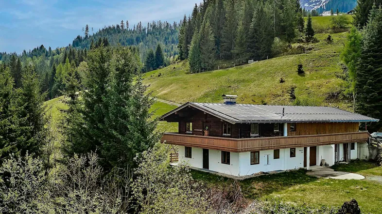 Traditionelles Chalet in den Bergen mit Holzbalkonen und umgeben von grünen Wäldern.