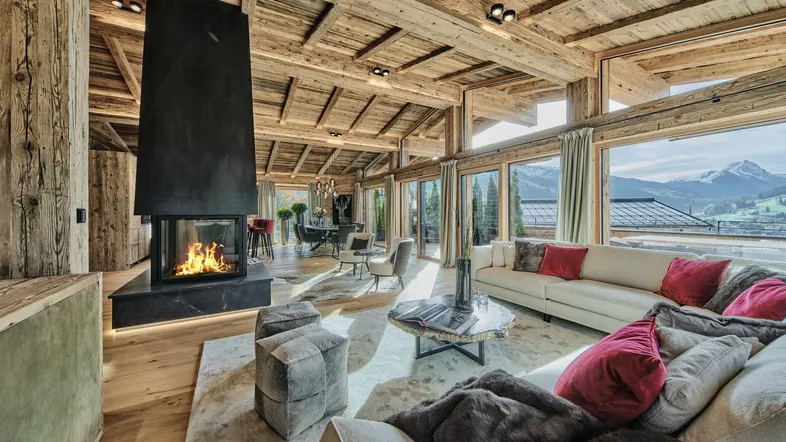 Großzügiges Wohnzimmer im Chalet-Stil mit Kamin, Holzbalkendecke und Panoramablick auf die Berge.