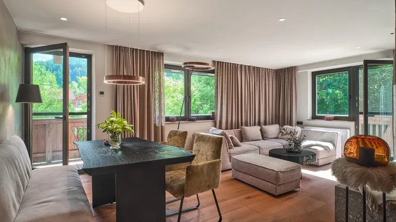 Helles Wohn- und Esszimmer mit Holzboden, gemütlicher Sitzecke und Zugang zu einem Balkon mit grüner Aussicht.