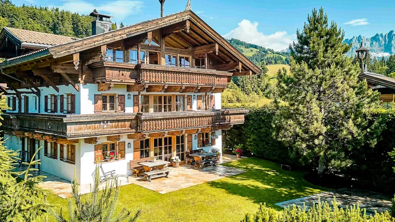 Traditionelles Chalet mit Holzbalkonen, gepflegtem Garten und Bergblick unter blauem Himmel.