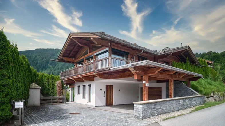 Traditionelles Holzchalet mit Carport und Balkonen, eingebettet in eine grüne Berglandschaft.