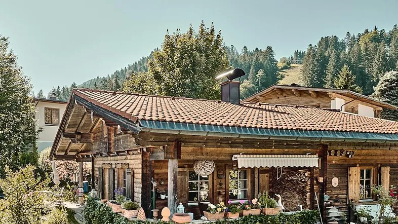 Traditionelles Holzhaus im Chalet-Stil mit Ziegeldach und üppiger Bepflanzung in alpiner Umgebung.