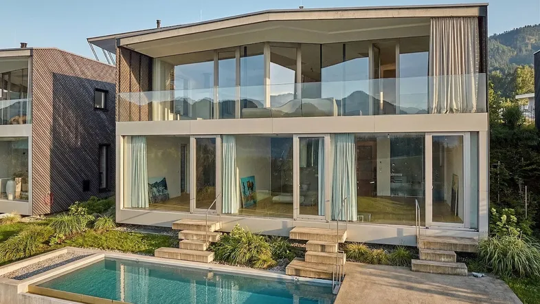 Moderne Villa mit Infinity-Pool und großen Glasfronten, umgeben von einer beeindruckenden Berglandschaft.