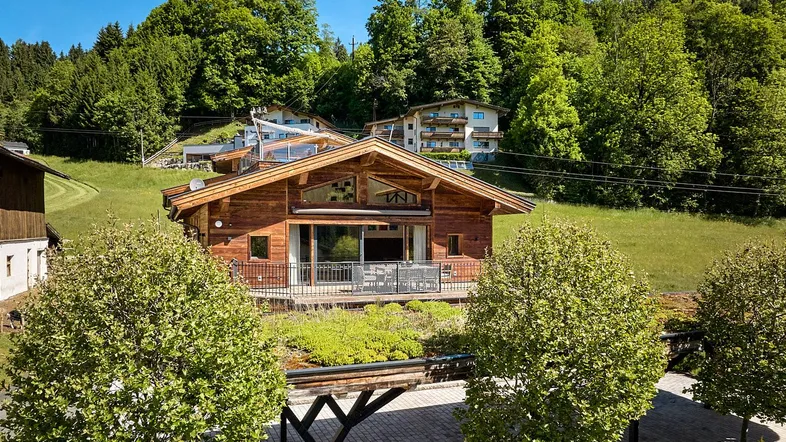 Charmantes Holzchalet in alpiner Umgebung mit grünen Hügeln und Wald im Hintergrund.