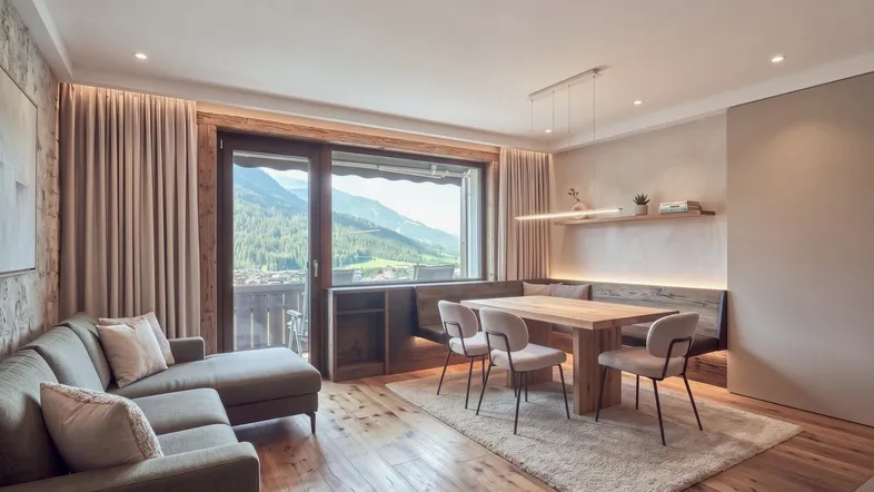 Gemütlicher Wohn- und Essbereich mit Holzboden, Bergblick und Zugang zum Balkon.