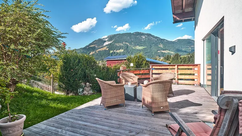 Geräumige Holzterrasse mit gemütlichen Korbmöbeln und herrlichem Bergblick in die Alpen.