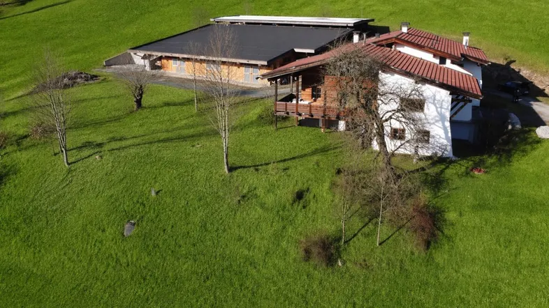 Luftaufnahme eines Anwesens mit traditionellem Haus und Nebengebäude in einer grünen Hügellandschaft.