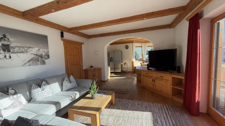 Helles Wohnzimmer mit Holzbalkendecke, gemütlichem Sofa und Zugang zum Essbereich.