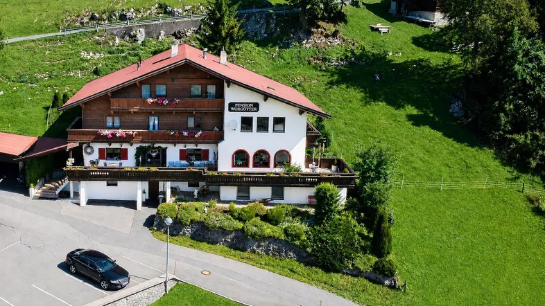Traditionelles Alpenhaus mit rotem Dach und Holzbalkonen, eingebettet in grüne Hügellandschaft.