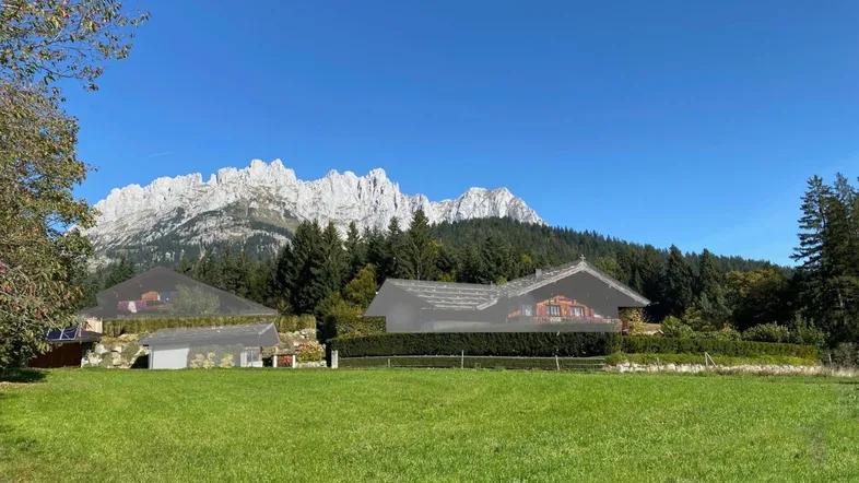 Weitläufige grüne Wiese mit Blick auf die majestätischen Berge und umliegende Häuser.