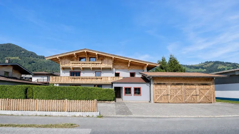 Hausfassade im alpinen Stil mit Holzbalkonen, großer Garage und Bergblick im Hintergrund.