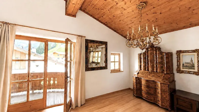 Geräumiges Wohnzimmer mit Holzbalkendecke, antiken Möbeln, Kronleuchter und Zugang zum Balkon.