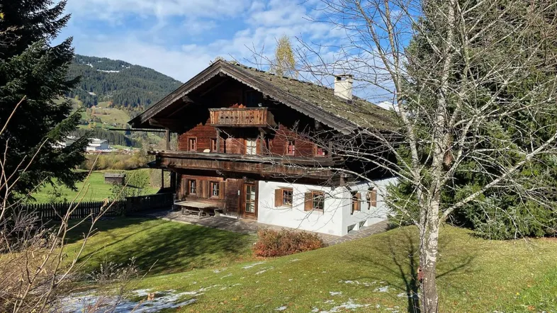 Traditionelles Holzhaus im alpinen Stil mit Satteldach und Balkonen, umgeben von grünen Wiesen und Bäumen.