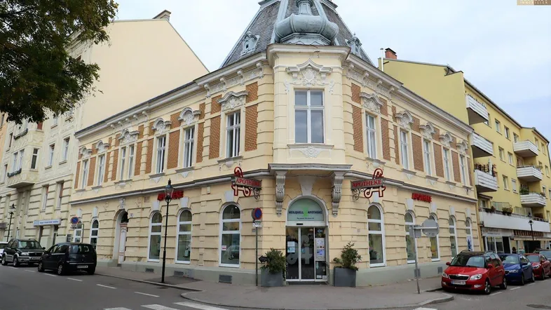 Historisches Eckgebäude mit Apotheke im Erdgeschoss und dekorativer Fassade an einer belebten Straße.