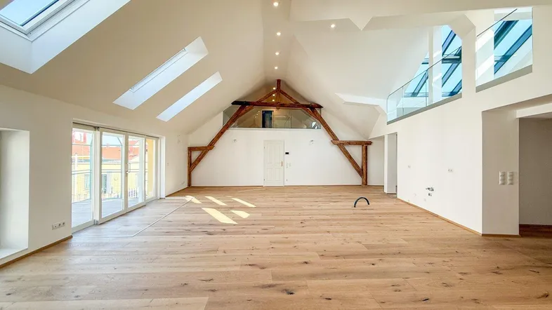 Großzügiger, heller Wohnbereich im Dachgeschoss mit Holzbalken, großen Fenstern und Zugang zum Balkon.