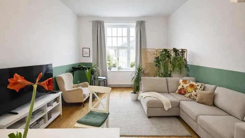 Helles Wohnzimmer mit beiger Eckcouch, Holzboden und grüner Akzentwand für eine gemütliche Atmosphäre.